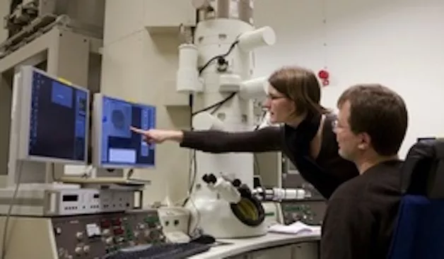 Two researchers looking at displays surrounded by technical equipment. Photo.